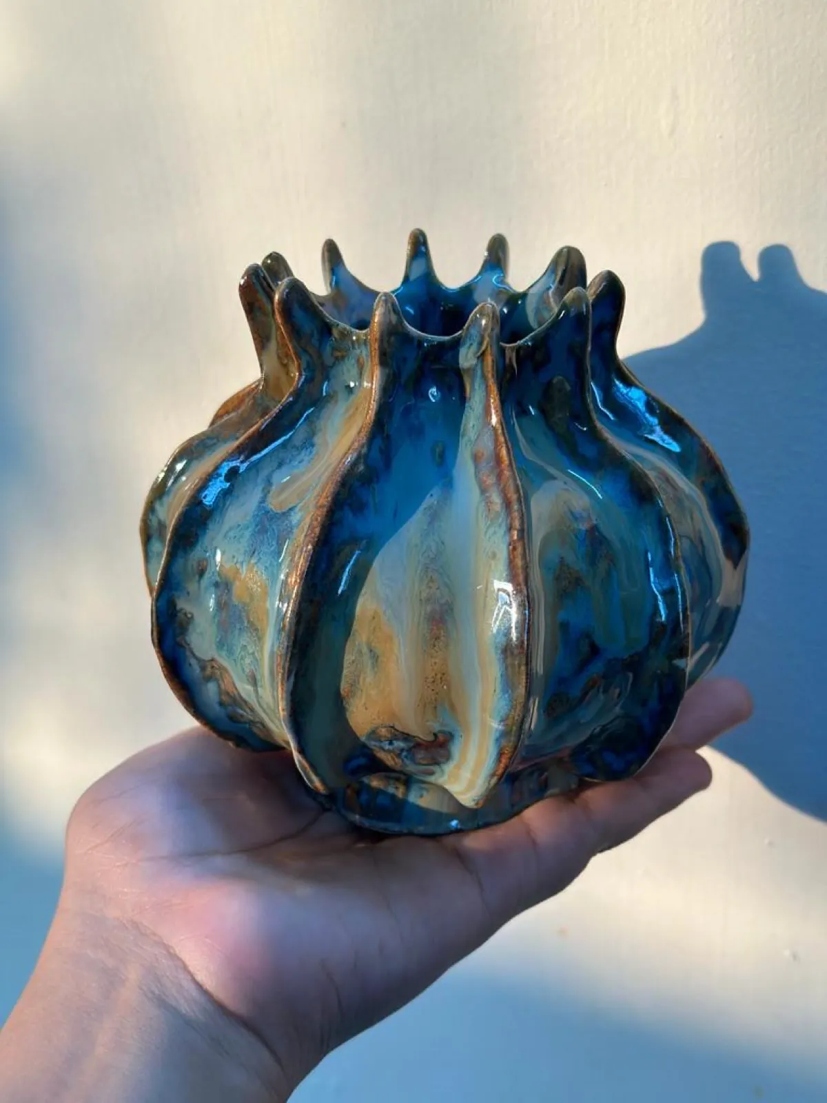 A fluted vase in a running blue and amber glaze, held in one hand